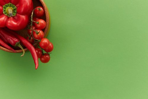 Free Red bell pepper, cherry tomatoes, and chili peppers on a green background, perfect for healthy eating concepts. Stock Photo