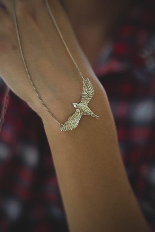 Person Holding Gold-colored Bird Pendant Necklace