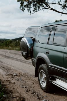 Green SUV with open trunk on a rural dirt road, perfect for travel and adventure.