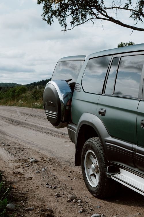 Free Green SUV with open trunk on a rural dirt road, perfect for travel and adventure. Stock Photo