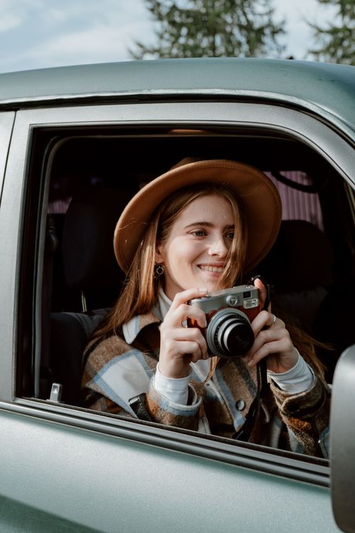 Free Young woman joyfully capturing moments with a camera from car. Stock Photo