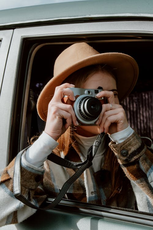 A Woman Wearing a Brown Fedora Hat Taking Photos Using a Camera