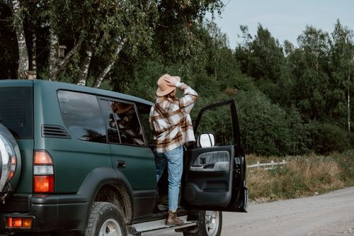 Free Person in plaid shirt standing by green SUV during a scenic road trip through nature. Stock Photo