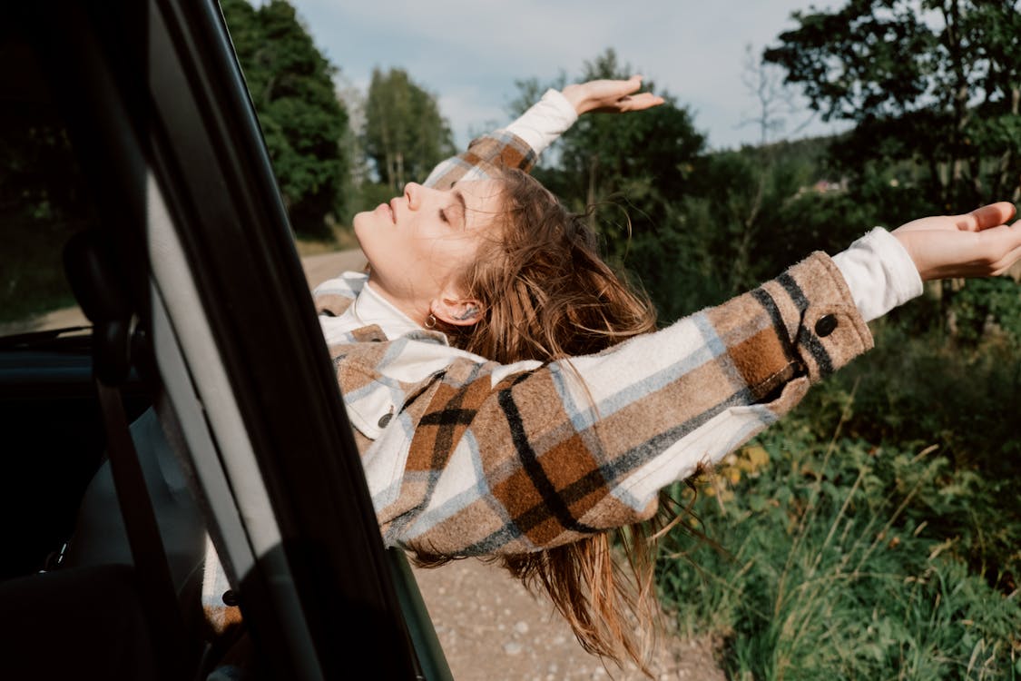 Woman Leaning from Car on Dirt Road in Forest