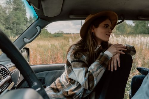 Free A woman in a plaid shirt smiles while sitting in a vehicle during a serene road trip. Stock Photo