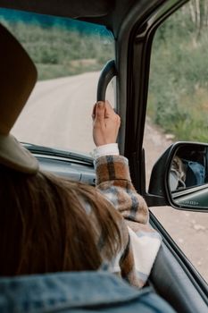 View from inside a car during a road trip with a woman holding the handle, showcasing a scenic outdoor background.