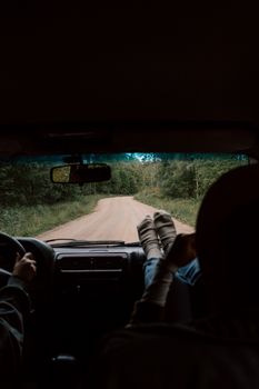 View from inside a car driving through a forested, unpaved road during the day.