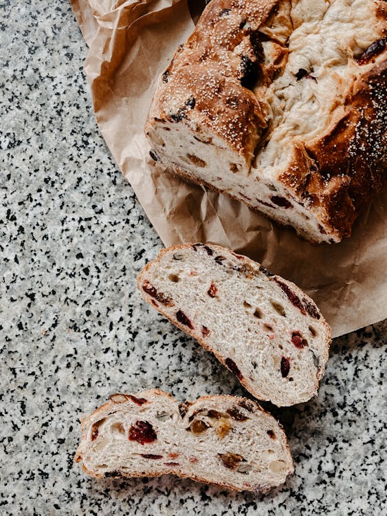 Free Top view freshly baked tasty multigrain bread with raisins and seeds cut on packing paper on gray table Stock Photo