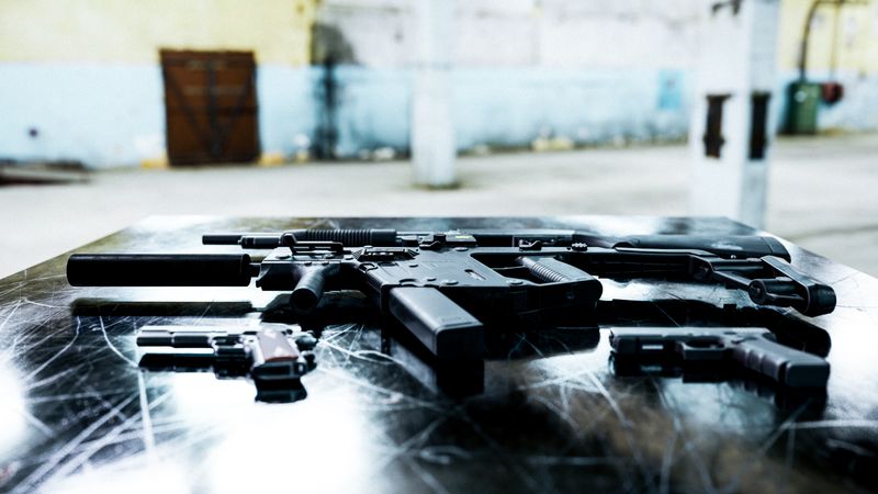 Various firearms displayed on a scratched metal table in an industrial setting.