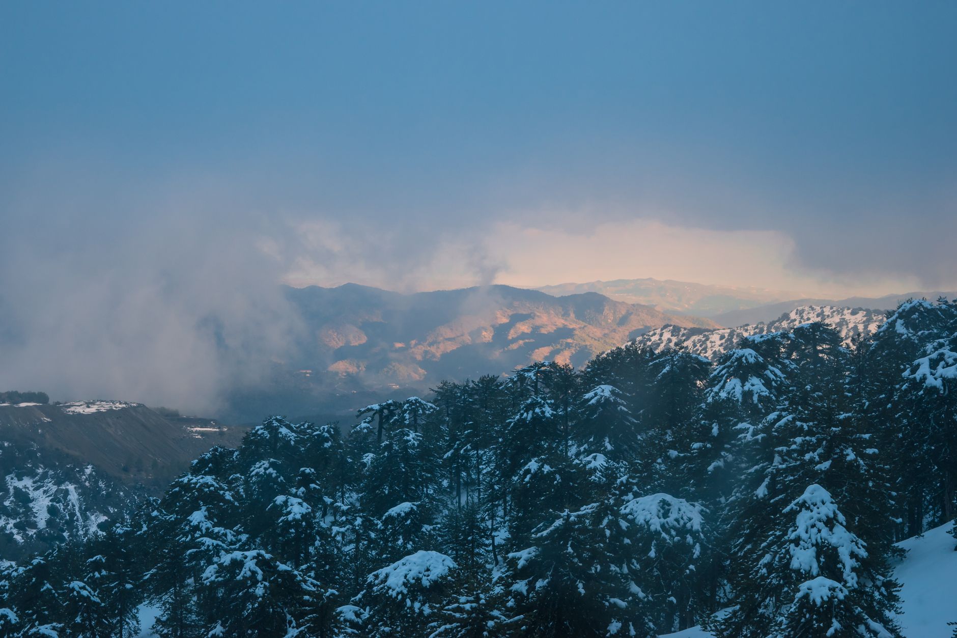 A breathtaking view of Troodos Mountains in Cyprus blanketed in snow under a sunrise sky.
