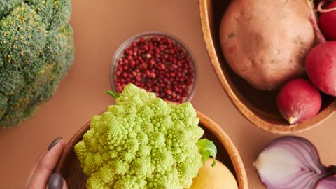 Hands holding fresh vegetables including Romanesco broccoli and potatoes, perfect for healthy cooking ingredients.