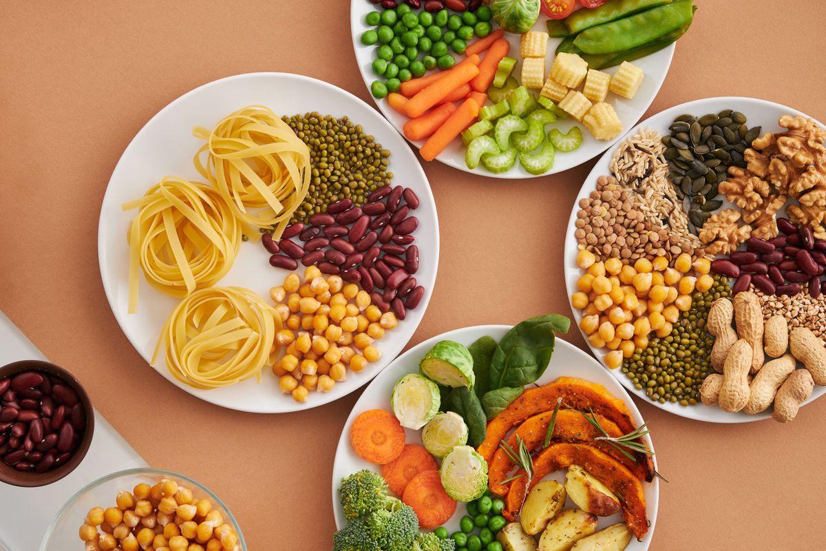 Plates of magnesium-rich foods on a warm background — legumes, chickpeas, pumpkin seeds, nuts, leafy greens and roasted vegetables.