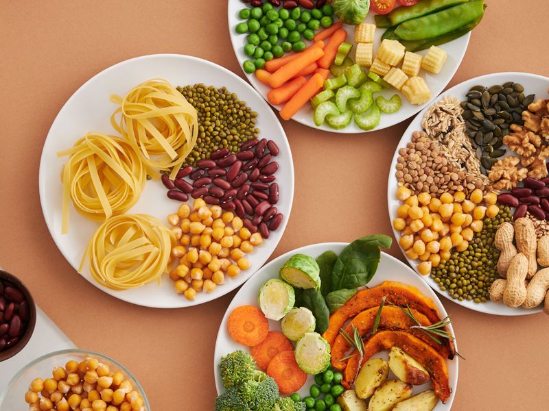 A vibrant mix of legumes, vegetables, nuts, and pasta arranged on white plates showcasing a balanced, healthy diet.