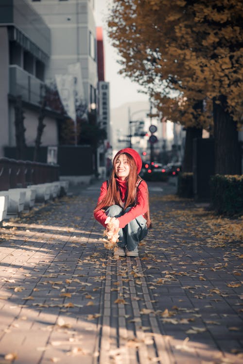 Woman in Red Jacket Sitting on Sidewalk