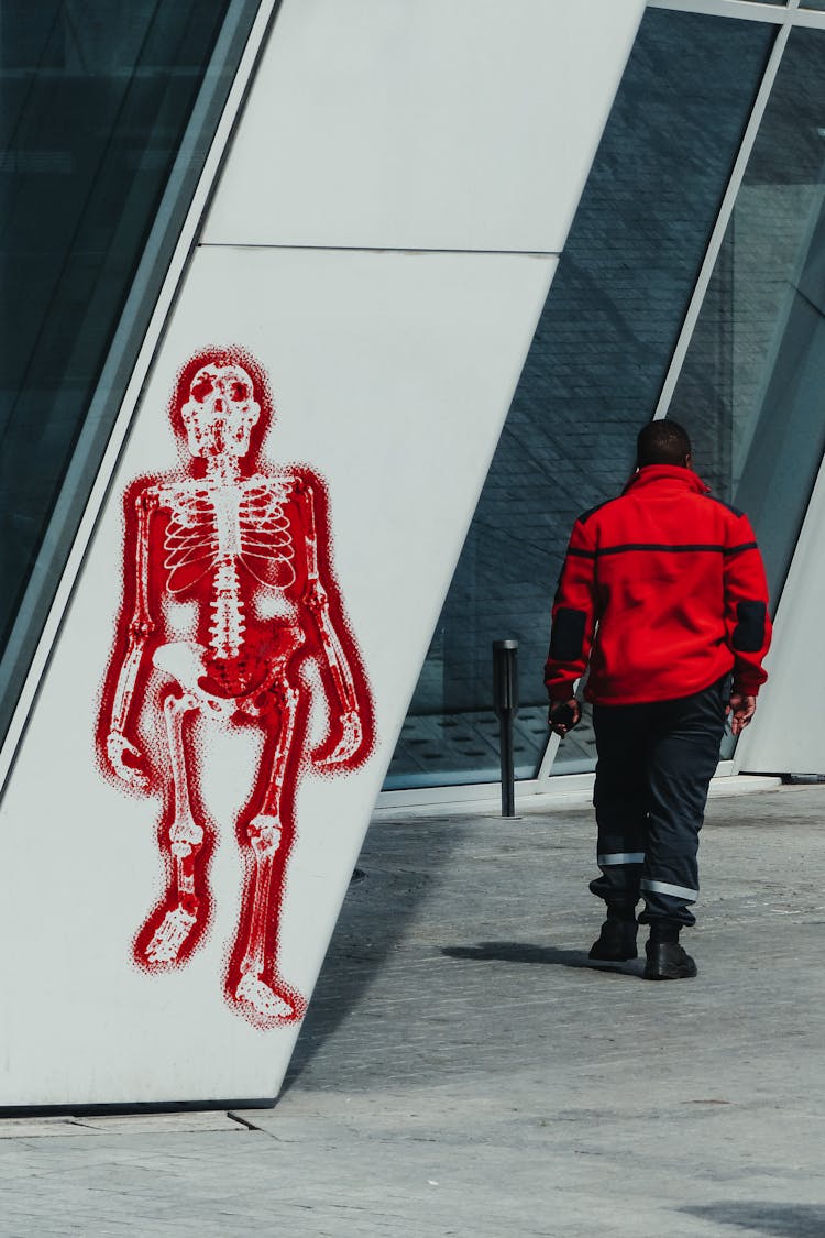 Man Walking Past Graffiti Of Skeleton On Wall