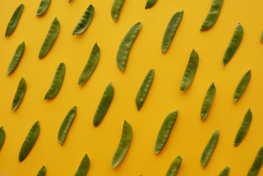 Flat lay of fresh green pea pods arranged on a vibrant yellow background, highlighting healthy eating.