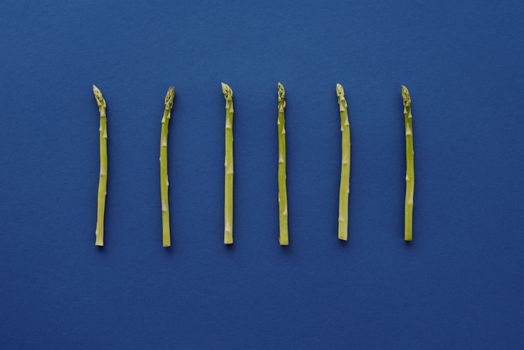 新鲜的绿色芦笋矛整齐地排列在生动的蓝色背景上，展现出简约与健康