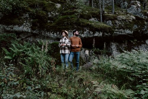Free A couple enjoys a nature walk through a lush, green forest, surrounded by rocks and ferns. Stock Photo