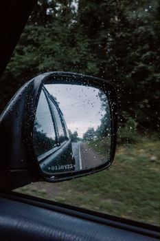 雨滴挂在汽车后视镜上，映出风景优美的道路，为旅途增添了几分变幻莫测的氛围