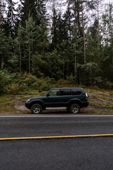 A lone SUV parked on a forest-lined roadside, perfect for travel themes.