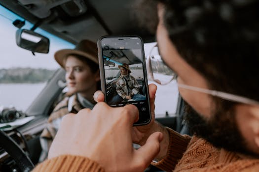 A man takes a photo of a woman in a car interior using a smartphone.