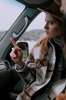 Woman in plaid jacket pointing while sitting inside a car, looking focused.