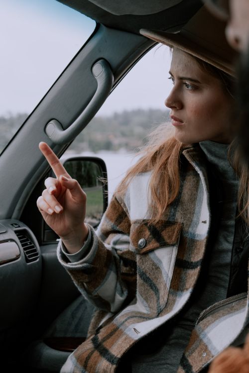Free Woman in plaid jacket pointing while sitting inside a car, looking focused. Stock Photo