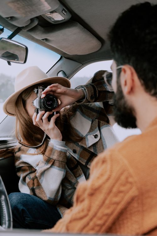 Free A couple capturing moments of their roadtrip adventure while sitting inside a car. Stock Photo