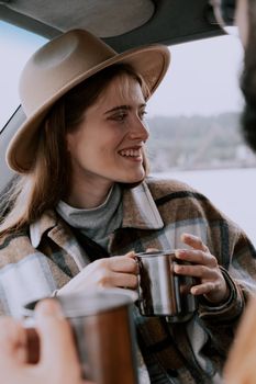 Cheerful woman in a hat enjoys a hot drink inside a vehicle.