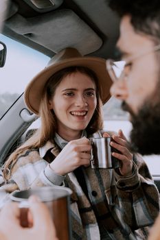 A couple shares a joyful moment drinking tea inside a car, showcasing warmth and togetherness.