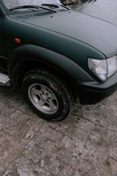Close-up of black SUV's front wheel parked by the waterside on a cloudy day.