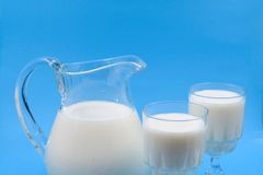 Creamy milk in a clear glass pitcher with two filled glasses against a blue background. Perfect for food photography.