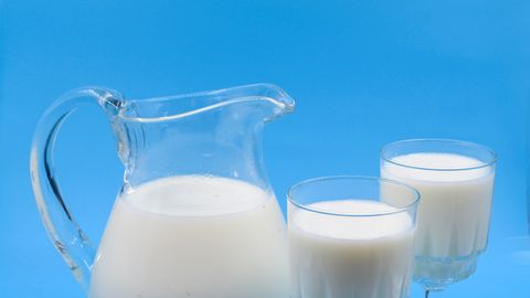 Creamy milk in a clear glass pitcher with two filled glasses against a blue background. Perfect for food photography.