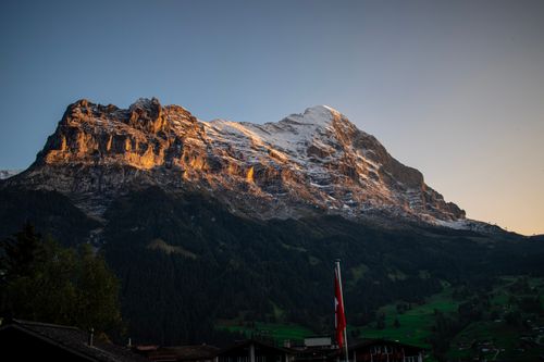 Free Captivating twilight view of the Swiss Alps with a national flag and lush greenery. Stock Photo
