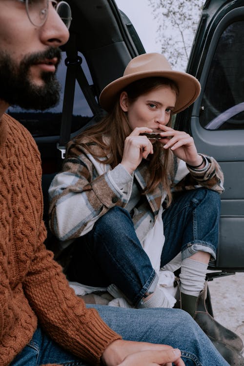 Woman in Blue Denim Jacket and Brown Hat Sitting on Car Seat