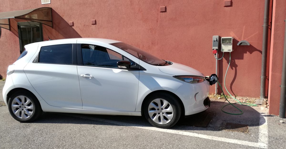 White electric vehicle charging at station against a red wall in San Bartolomeo di Breda di Piave, Italy.