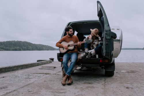 Free A couple enjoys a road trip by the seaside, playing guitar and relaxing together. Stock Photo