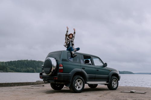 Woman Raising her Hands on Top of a Car