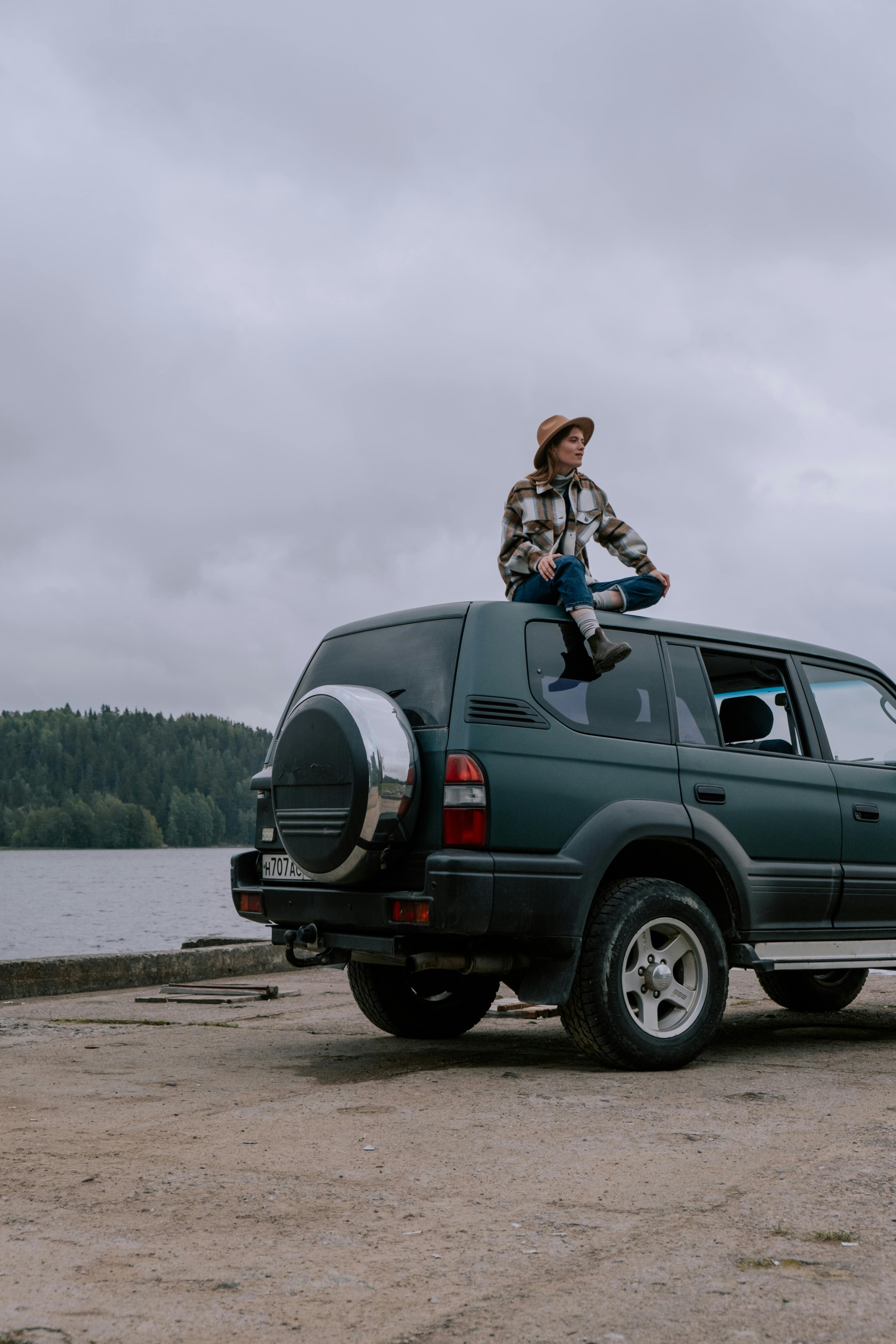 A woman sits atop an SUV by a serene lake during an outdoor adventure.