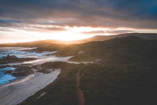 A stunning aerial view of a rugged coastline during sunset with waves crashing on the shore.