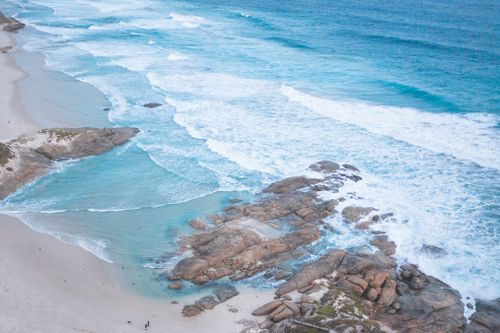 Free Drone shot capturing turquoise waters and rugged rocks along a scenic shore. Stock Photo