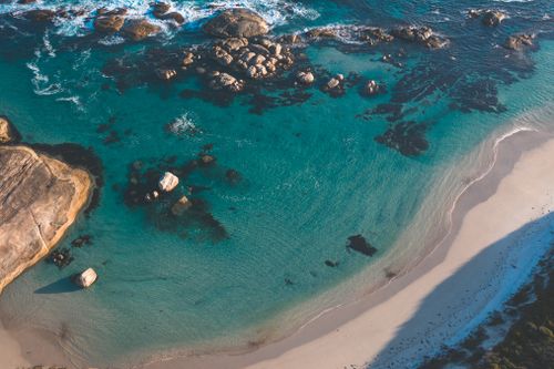 Free Stunning aerial view of a tranquil beach with turquoise waters and rocky formations along the shoreline. Stock Photo