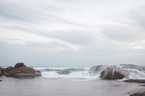 Stormy sea splashing on wet coast with rough stones against overcast cloudy sky in nature on seaside with horizon line