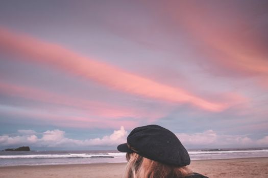 一个女人在宁静的海滩上，戴着一顶帽子看日落