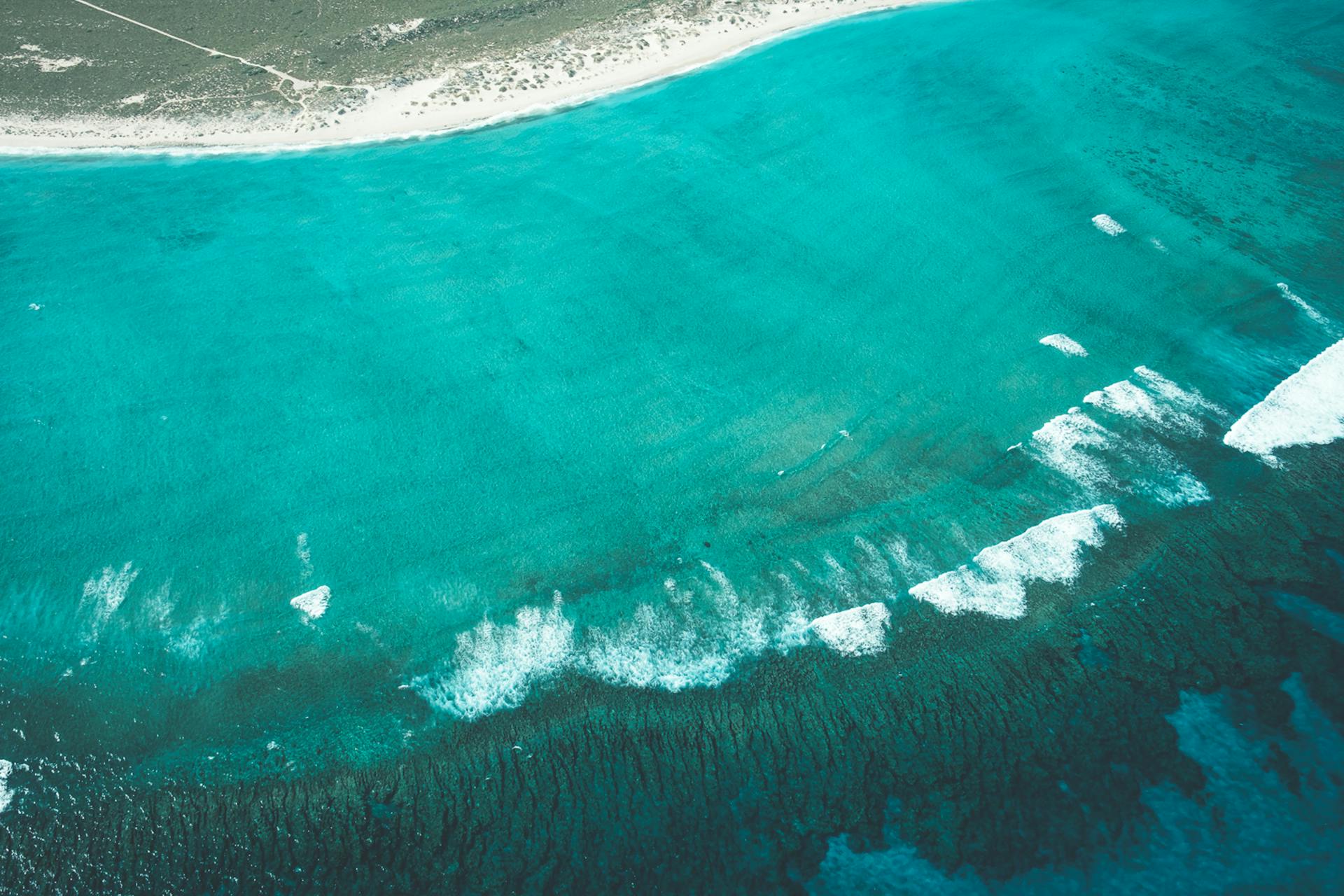 Drone view of turquoise water of ocean with foam and ripples near sandy shore