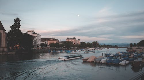 Rippling river with motorboats near embankment of city against buildings under cloudy sky