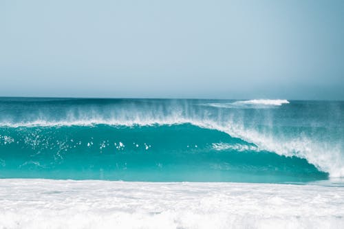 Stormy tide of turquoise ocean splashing near foamy water against cloudless sky in nature on summer day in tropical resort