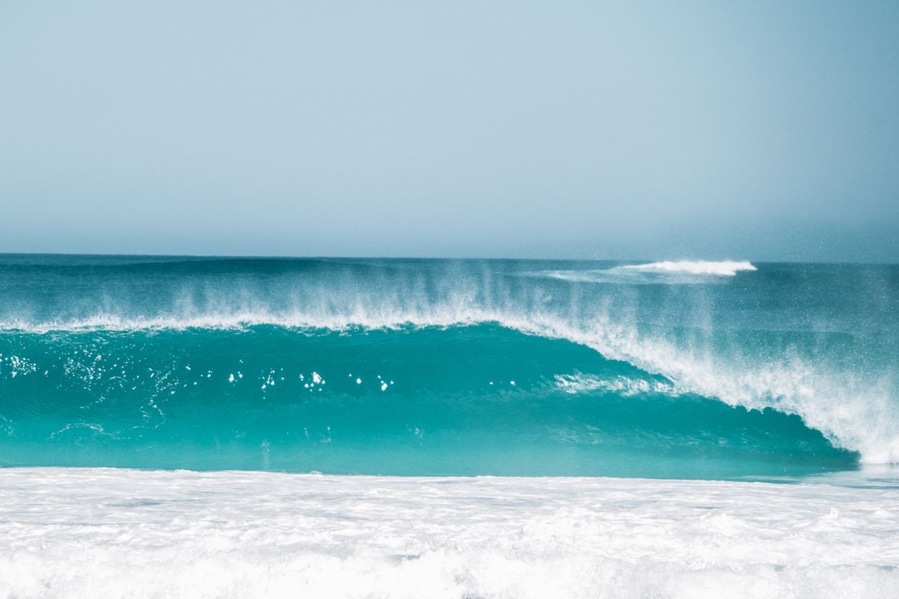 stormy tide of turquoise ocean splashing near foamy water against clou