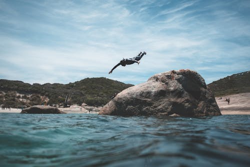 Unrecognizable man jumping into blue sea