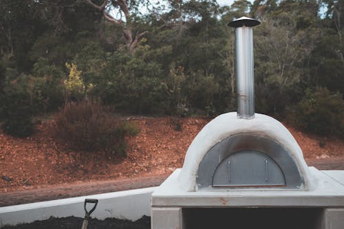 Stone pizza oven with stainless flue placed in lush summer garden for picnic